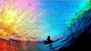 A vibrant image of a colorful wave with a silhouette of a person surfing, showcasing a blend of blues, purples, and oranges in the water and sky.