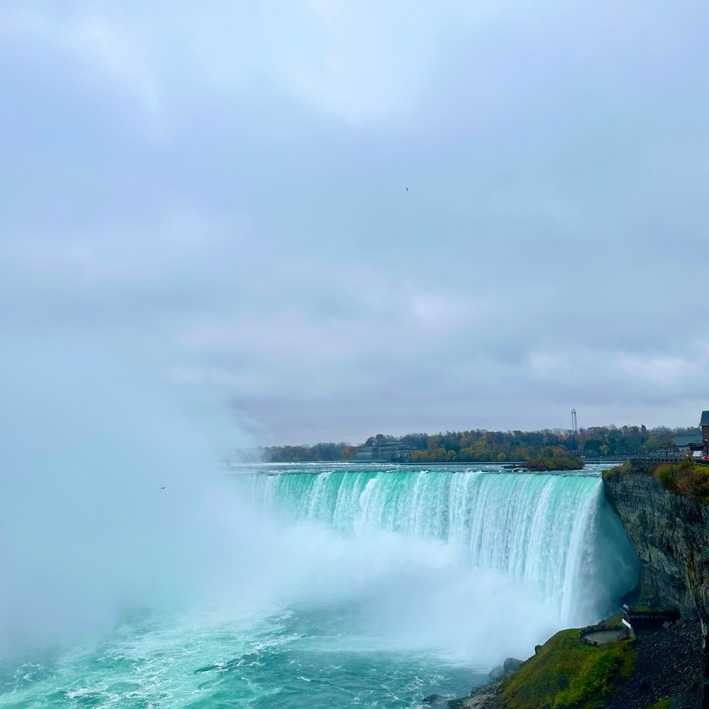 A view of Niagara Falls showing the cascading water surrounded by mist under a cloudy sky.