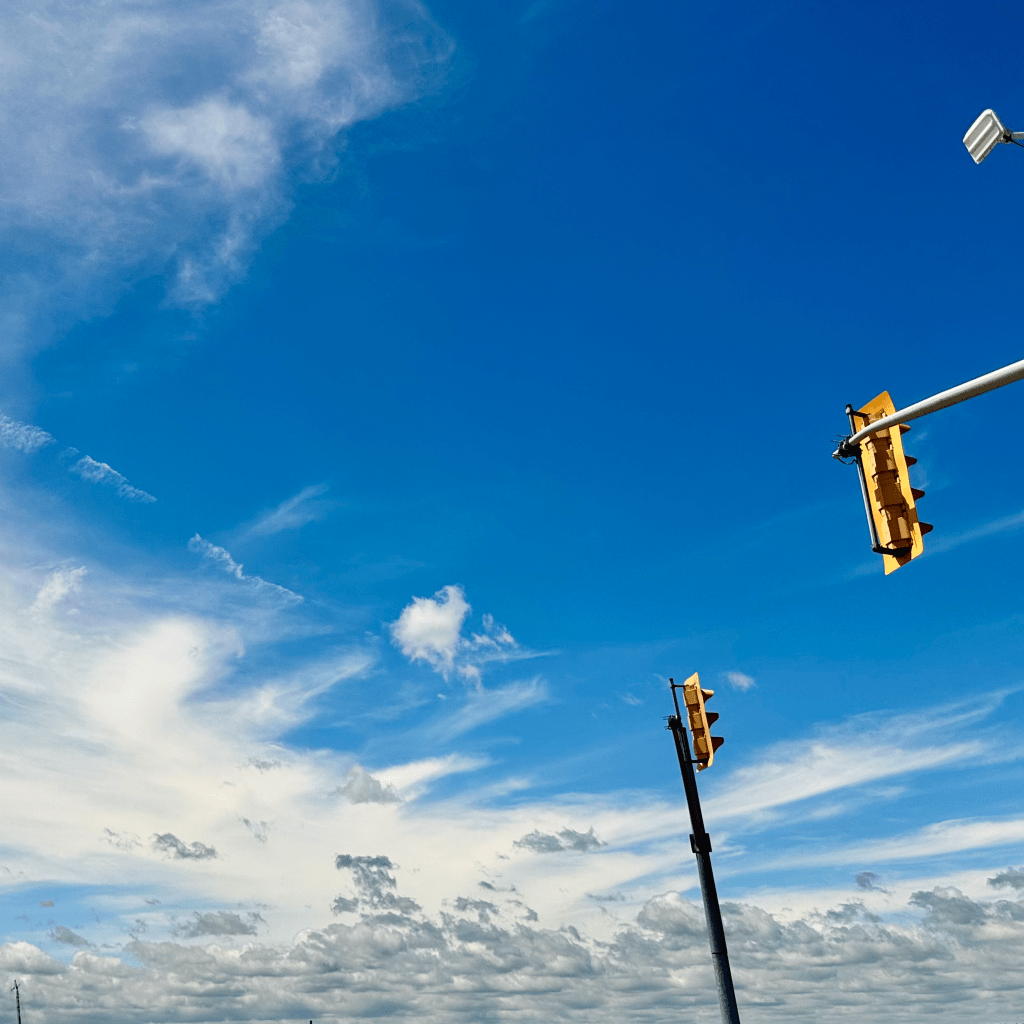 A clear blue sky with wispy clouds and traffic lights in the foreground.